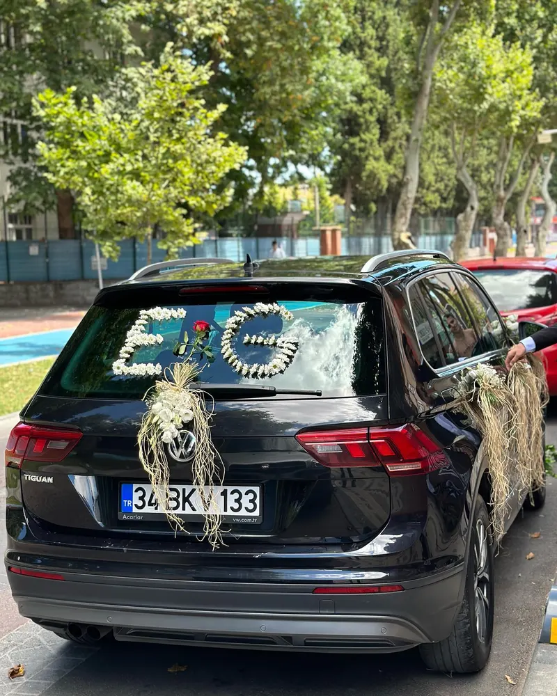 Arka camında çiçekten baş harfler bulunan siyah SUV nişan arabası